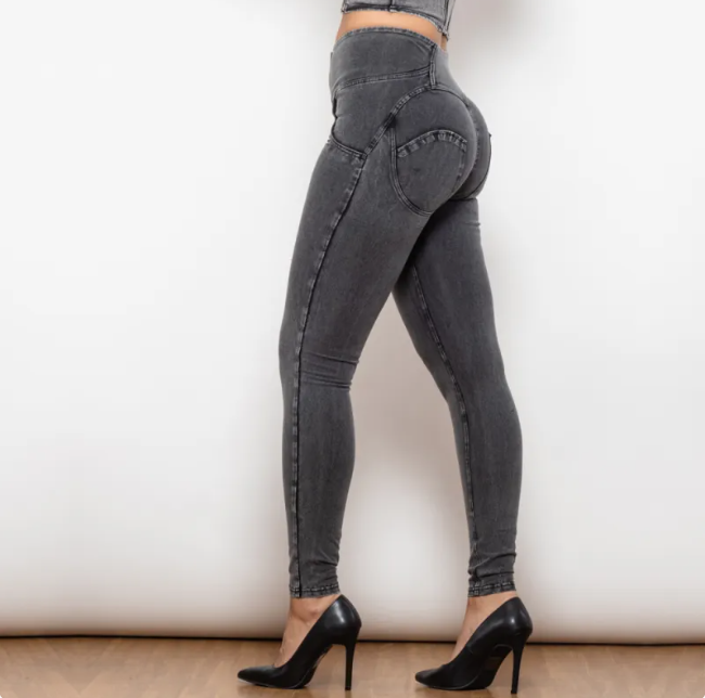 Person wearing gray high-waisted jeans and black high-heeled shoes on a plain background