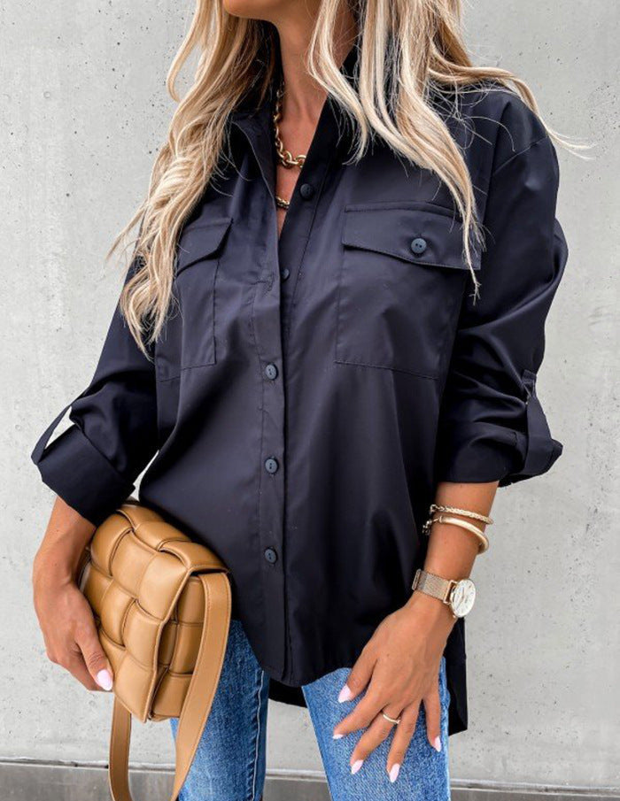 Person wearing a black button-up shirt and blue jeans, holding a tan handbag against a gray background