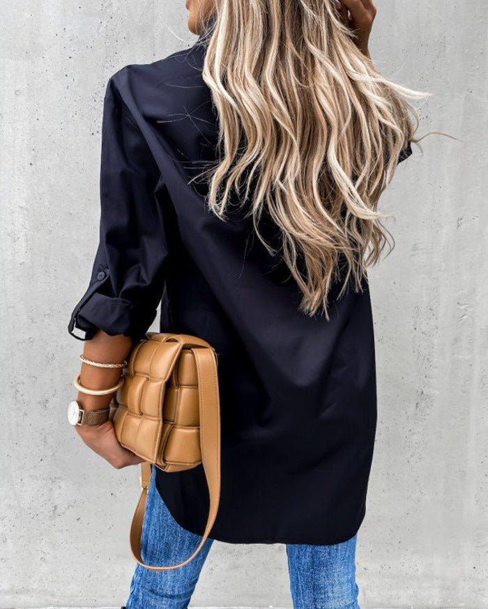 Person wearing a black coat and blue jeans, holding a tan backpack against a gray wall.