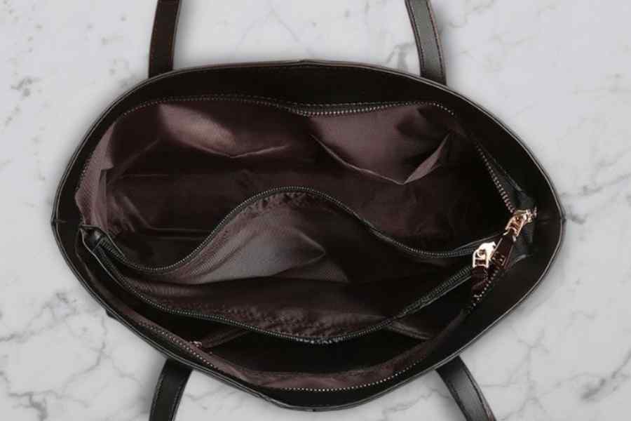Black handbag with open zipper on a marble surface
