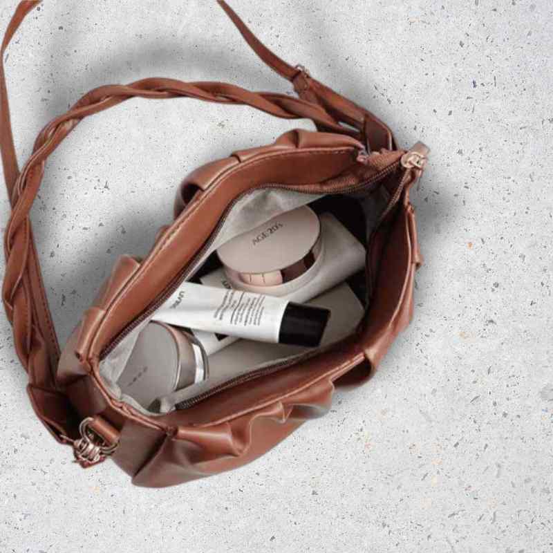 Brown leather bag with skincare products on a light gray background