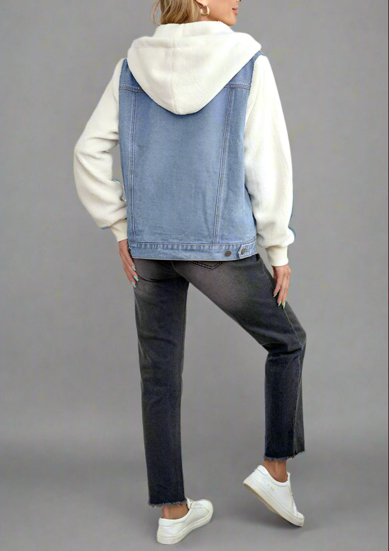 Woman wearing a denim vest over a white hoodie in a bedroom setting