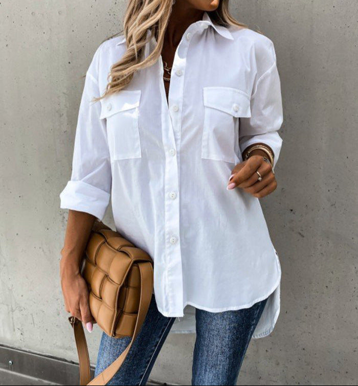 Woman wearing a white shirt and sunglasses, standing against a gray wall.