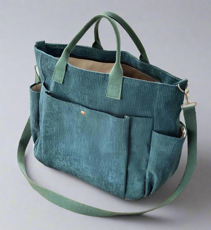 Teal tote bag with multiple pockets and a shoulder strap on a light gray background