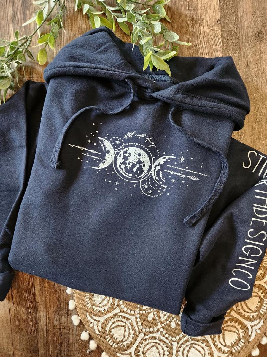 Navy blue hoodie with celestial design on a wooden surface