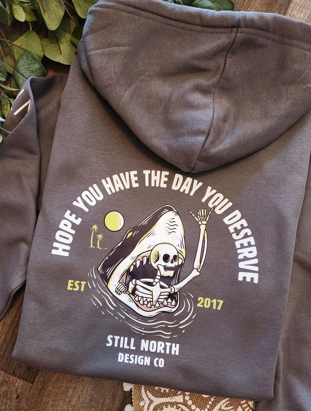 Gray hoodie with a graphic design and text on a wooden surface