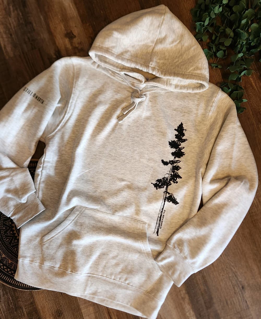 Beige hoodie with a black tree design on a wooden surface