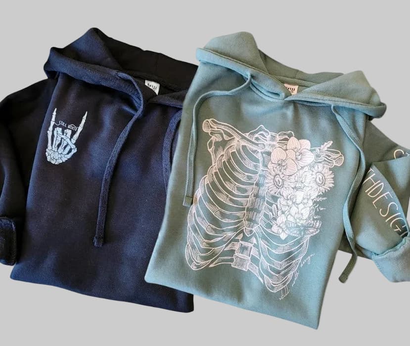 Two hoodies, one navy and one green, with artistic designs on a gray background