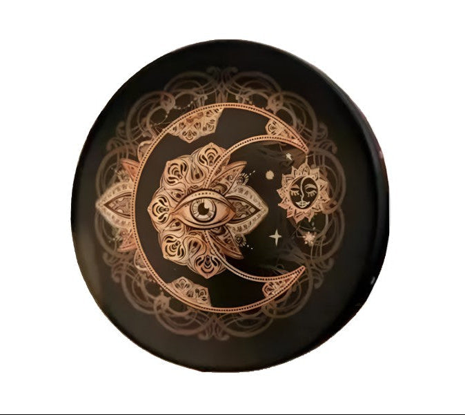 Decorative plate with intricate designs including a moon, eye, and star on a black background.
