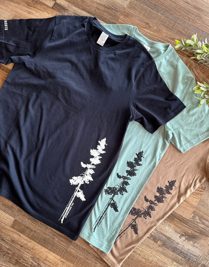 Three t-shirts, one black and one light blue, with tree designs on a wooden surface.